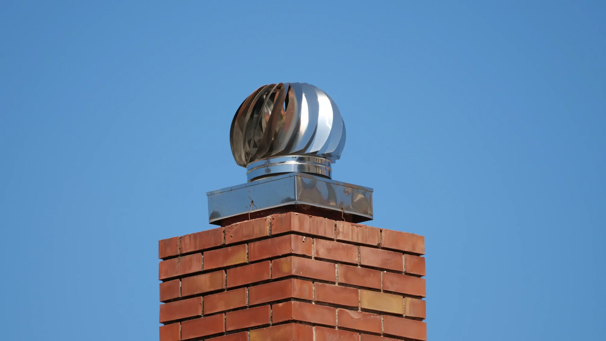 Metal chimney stack with a rotating vent against a clear blue sky