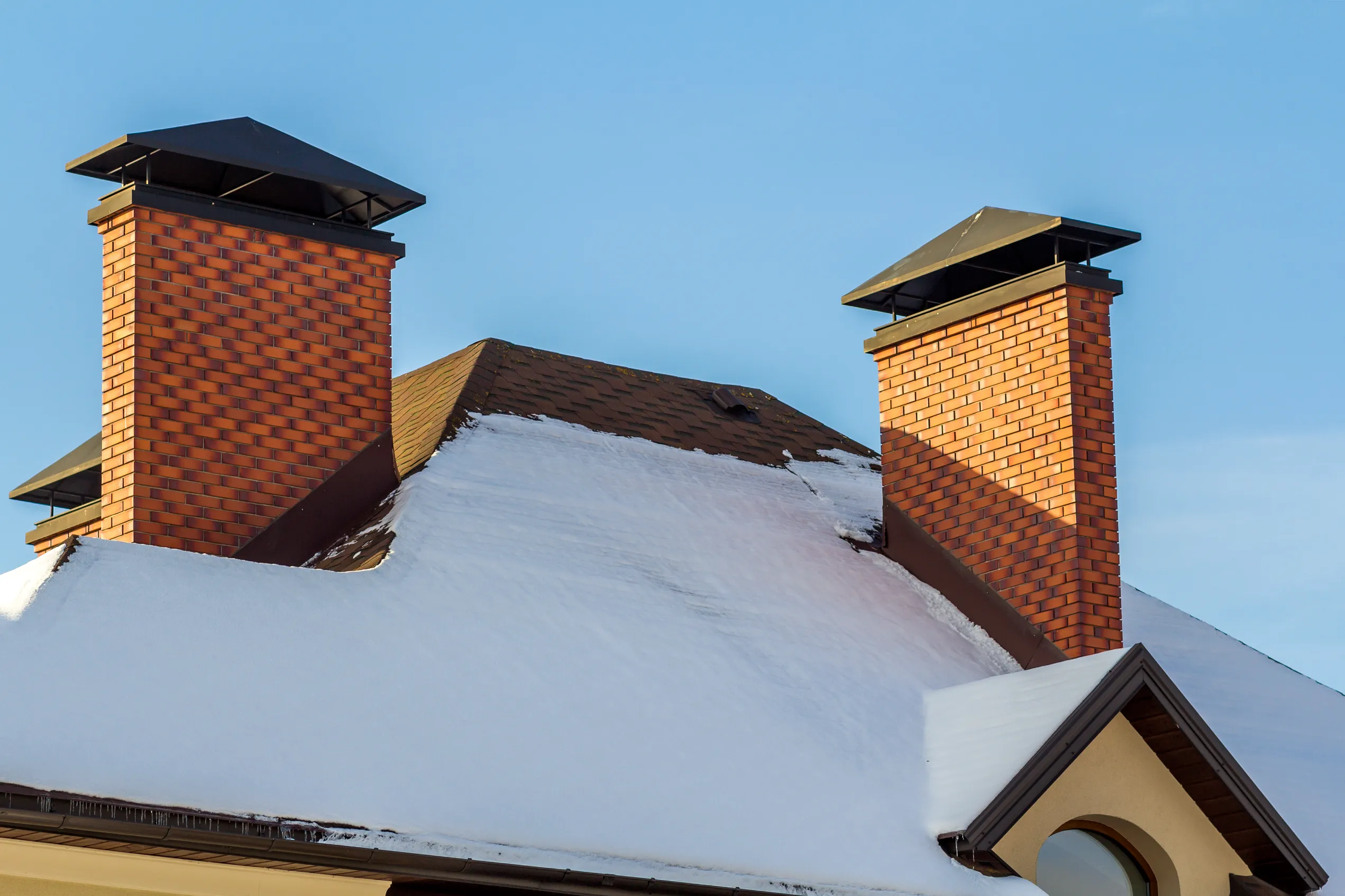 Snowy rooftop with brick chimneys against a blue sky